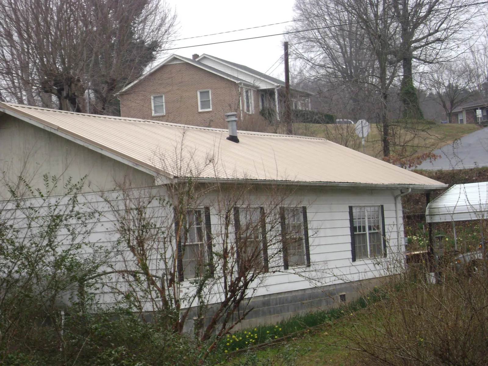 Tan metal roof on a white sided house set into a hillside — Commercial Roofing by Roofing Brothers in Margate City
